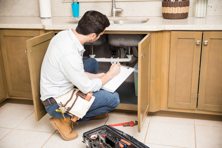 Plumber inspecting pipes under a kitchen sink using a wrench.