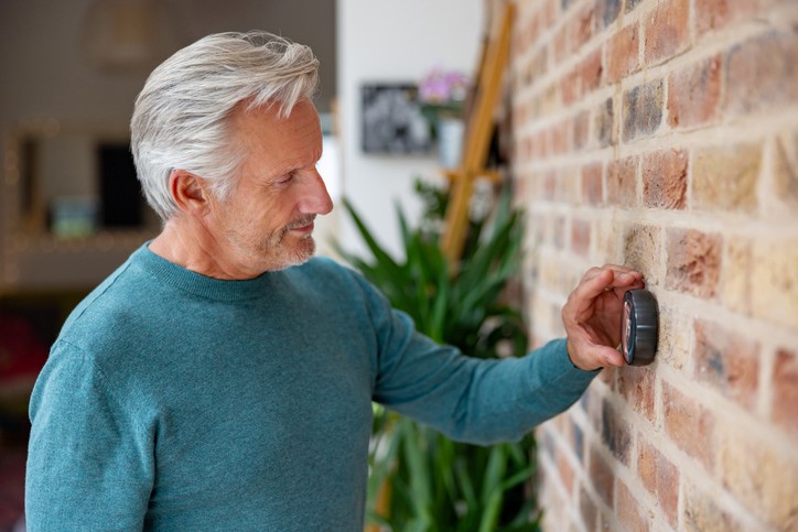Man adjusting smart thermostat on brick wall