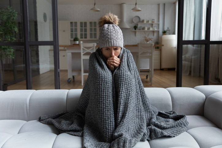 Girl in shawl feeling cold at home, highlighting need for heating system tune-up