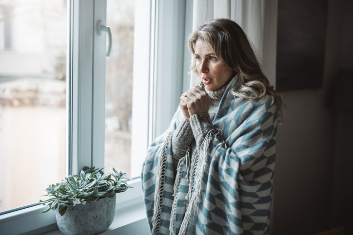 Girl wrapped in a blanket feeling cold indoors while home heating system runs during the day.