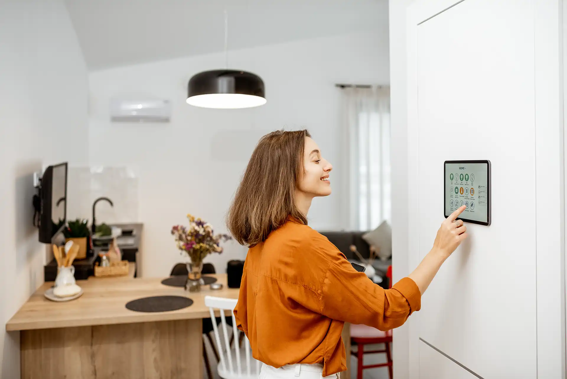 Woman using smart home thermostat panel on wall in modern kitchen