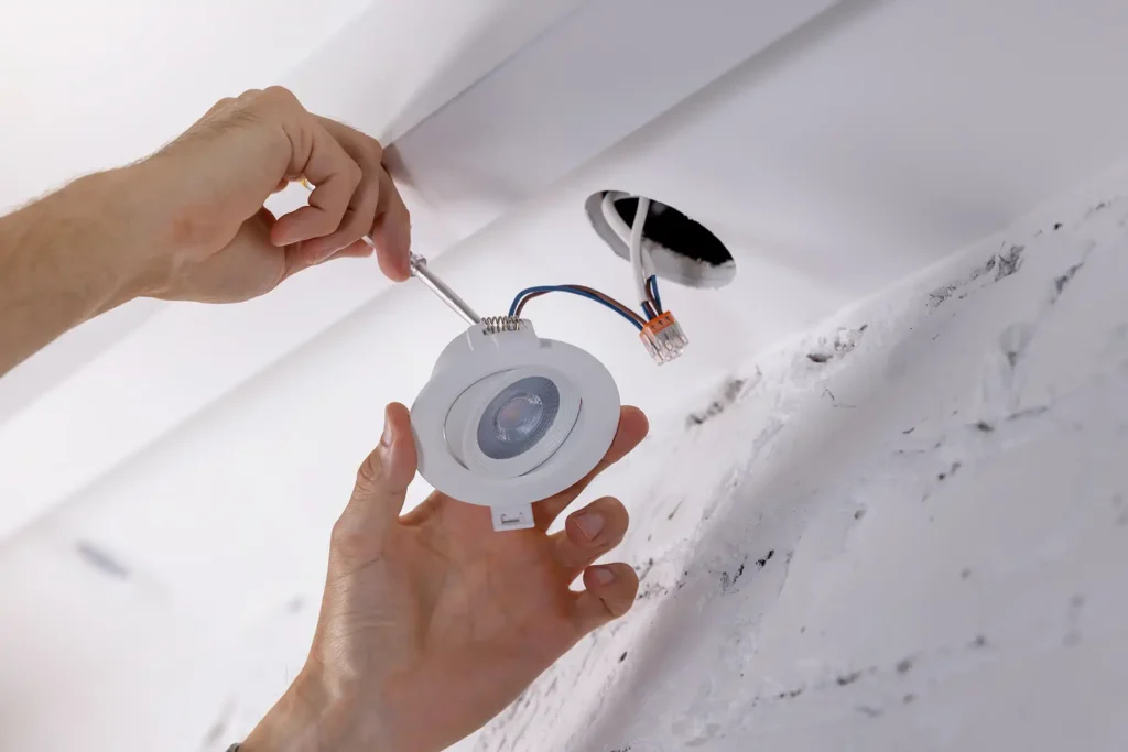 Electrician installing recessed LED light fixture in ceiling
