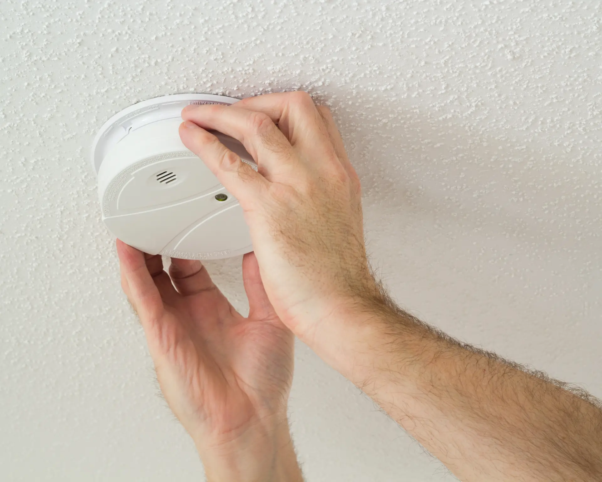 Close-up of hands installing a smoke detector on a white ceiling