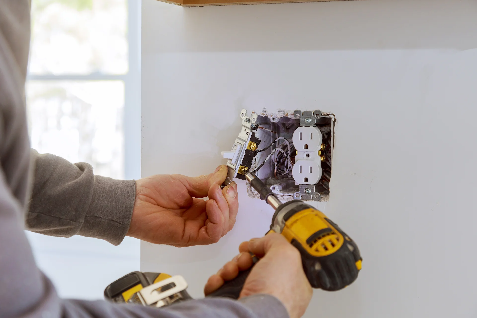 Electrician installing an electrical outlet in a wall using a power drill